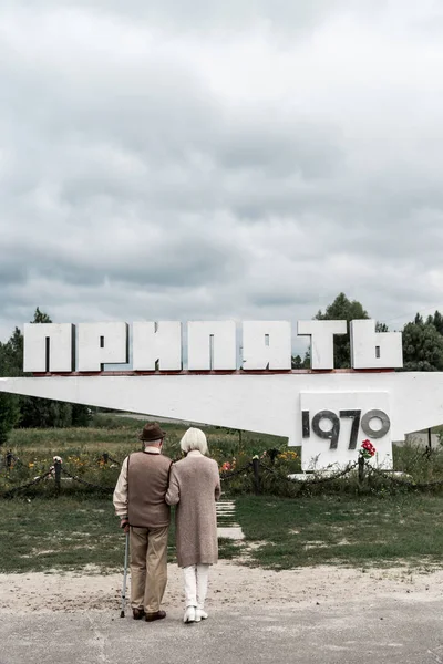 PRIPYAT, UKRAINE - AUGUST 15, 2019: back view of retired husband and wife standing near monument with pripyat letters — Stock Photo