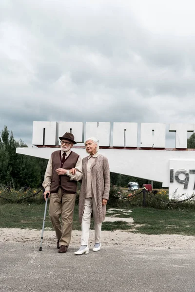 PRIPYAT, UCRANIA - 15 de agosto de 2019: Pareja jubilada caminando cerca del monumento con letras pripyat - foto de stock