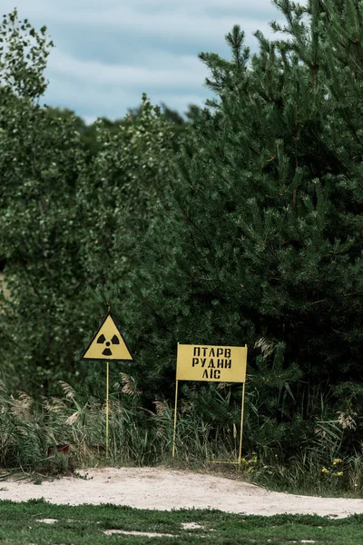 PRIPYAT, UCRANIA - 15 de agosto de 2019: zona de chernobil con señales de advertencia amarillas cerca de árboles verdes - foto de stock