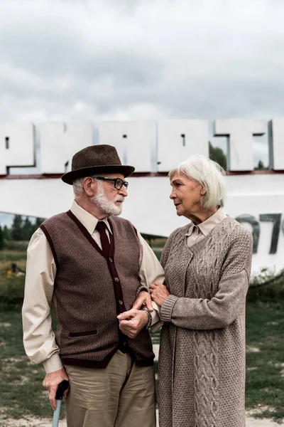 PRIPYAT, UKRAINE - AGOSTO 15, 2019: casal aposentado olhando um para o outro perto do monumento com letras pripyat — Fotografia de Stock