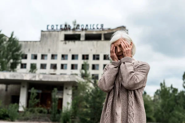 Прип'ять, Україна-15 серпня 2019: старша жінка прикриваючи обличчя біля будівлі з готелем «Поліський напис» в Чорнобилі — Stock Photo