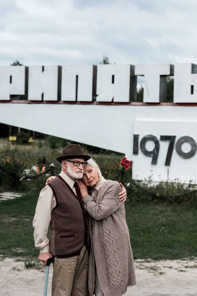 PRIPYAT, UKRAINE - 15 AOÛT 2019 : couple de personnes âgées embrassant près du monument avec des lettres pripyat — Photo de stock