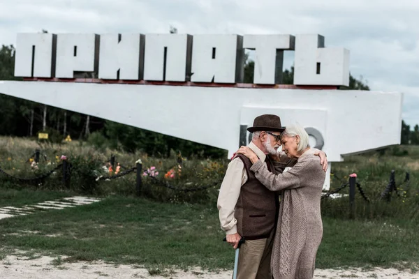 PRIPYAT, UCRAINA - 15 AGOSTO 2019: pensionati che si abbracciano vicino al monumento con lettere di pripiato — Foto stock