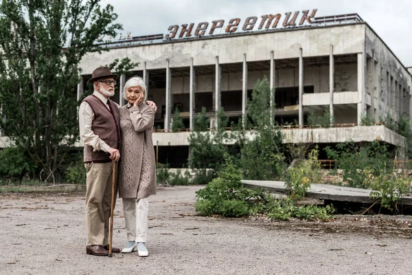 Pripjat, Ukraine - 15. August 2019: Rentnerehepaar steht in Tschernobyl neben Gebäude mit energetischem Schriftzug — Stockfoto