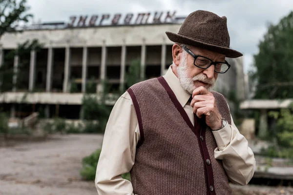 Pripjat, Ukraine - 15. August 2019: Nachdenklicher älterer Mann steht in Tschernobyl vor einem Gebäude mit energiegeladenen Schriftzügen — Stockfoto
