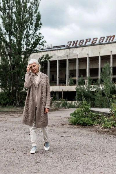 Прип'ять, Україна-15 серпня 2019: старша жінка, що йде біля будівлі з енергійною напис в Чорнобилі — стокове фото