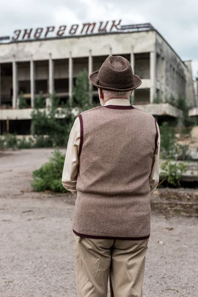 Прип'ять, Україна-15 серпня 2019: назад погляд старших людини в капелюсі стоїть біля будівлі з енергійною напис в Чорнобилі — стокове фото