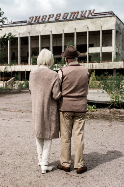 PRIPYAT, UCRÂNIA - AGOSTO 15, 2019: visão traseira do casal aposentado em pé perto do prédio com letras energéticas em chernobyl — Fotografia de Stock