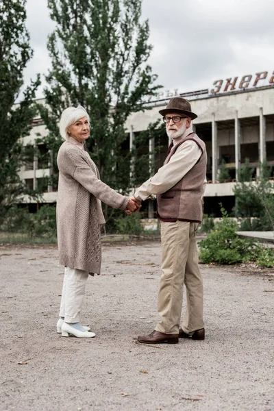 PRIPYAT, UKRAINE - 15 AOÛT 2019 : couple de personnes âgées se tenant la main près du bâtiment avec un lettrage énergique à Tchernobyl — Photo de stock