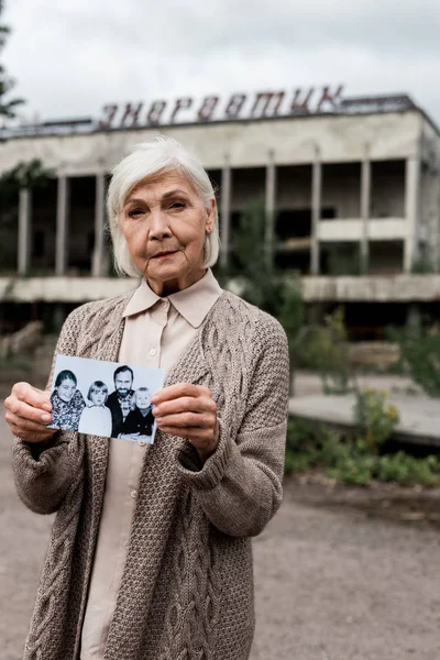 PRIPYAT, UCRAINA - 15 AGOSTO 2019: anziana donna che tiene foto vicino all'edificio con lettere a Chernobyl — Foto stock