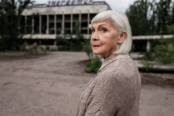 PRIPYAT, UCRANIA - 15 de agosto de 2019: mujer mayor mirando la cámara cerca del edificio en Chernobyl - foto de stock