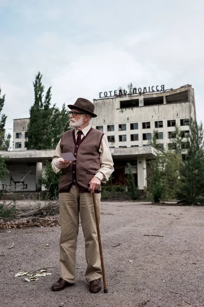 PRIPYAT, UKRAINE - 15 AOÛT 2019 : homme âgé avec canne à pied tenant une photo près du bâtiment avec des lettres polissya de l'hôtel — Photo de stock