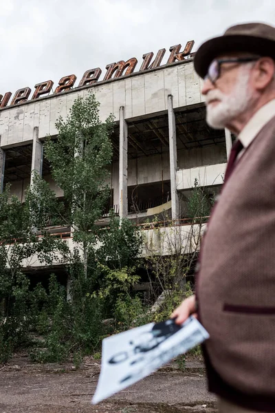 PRIPYAT, UCRAINA - 15 AGOSTO 2019: focus selettivo della costruzione con lettering senior man holding photo — Foto stock