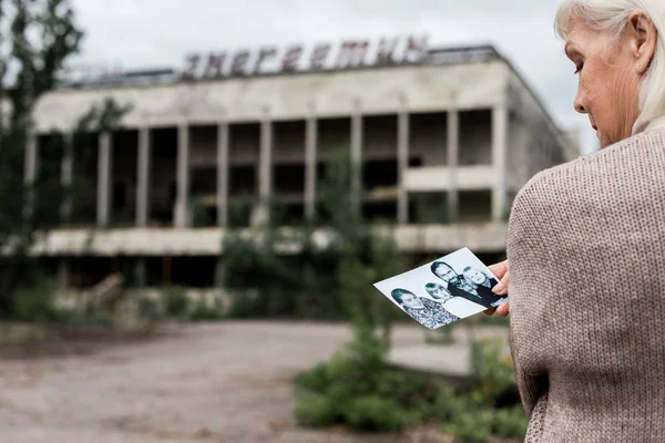Pripjat, ukraine - 15. August 2019: selektiver Fokus einer Frau mit grauen Haaren mit Foto in der Nähe eines Gebäudes mit Schriftzug in Tschernobyl — Stockfoto