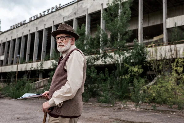 PRIPYAT, UCRANIA - 15 de agosto de 2019: un hombre mayor con foto cerca de un edificio en Chernobyl - foto de stock