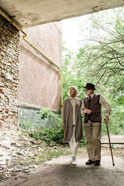 Retired woman and senior man with walking stick walking near green trees — Stock Photo