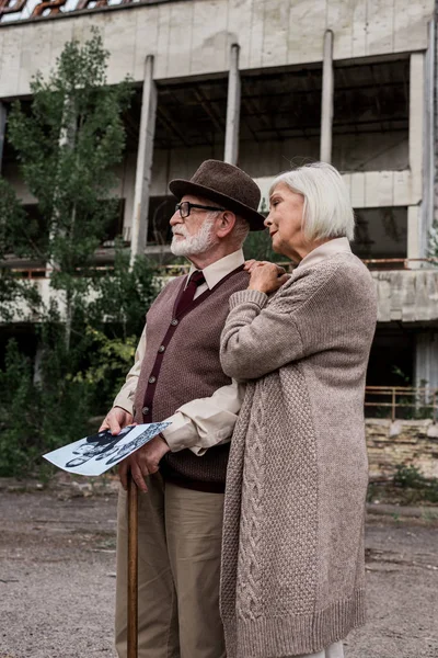 PRIPYAT, UKRAINE - AUGUST 15, 2019: retired man and woman holding black and white photo near building — Stock Photo