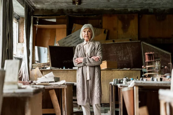 Selektiver Fokus einer Rentnerin, die mit verschränkten Armen an schmutzigen Tischen steht — Stockfoto