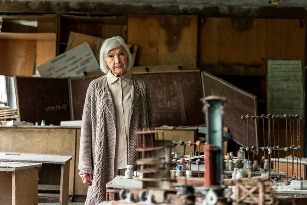 Selektiver Fokus einer Rentnerin, die an schmutzigen Tischen im Klassenzimmer steht — Stockfoto