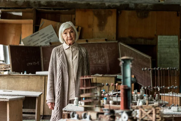 Selective focus of retired woman standing near dirty tables in classroom — Stock Photo