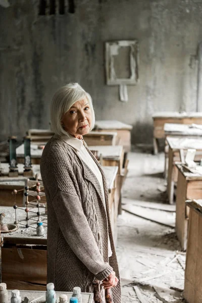 Triste femme retraitée avec les cheveux gris debout dans la salle de classe sale — Photo de stock