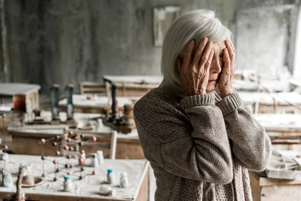 Rentnerin berührt Gesicht und steht in schmutzigem Klassenzimmer — Stockfoto