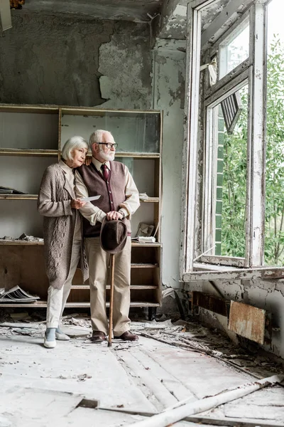 Rentnerpaar blickt auf Fenster, während es in beschädigtem Klassenzimmer steht — Stockfoto