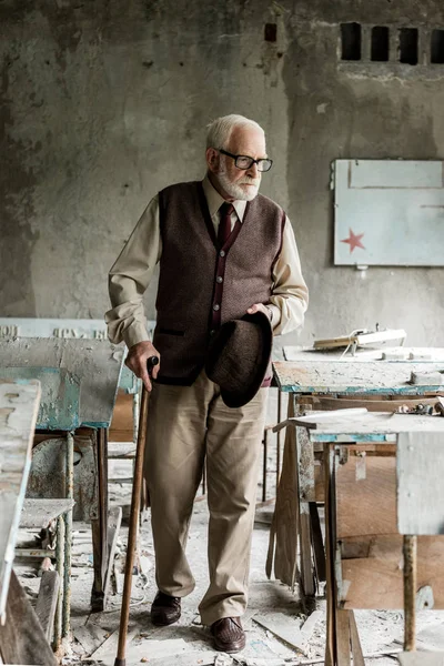 Selective focus of retired man walking near damaged tables in school — Stock Photo