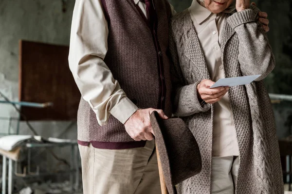 Обрезанный вид пары пенсионеров, стоящей в заброшенной школе и держащей фотографию — стоковое фото