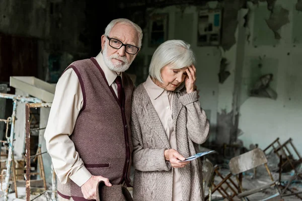 Retired couple standing in abandoned school and holding photo — Stock Photo