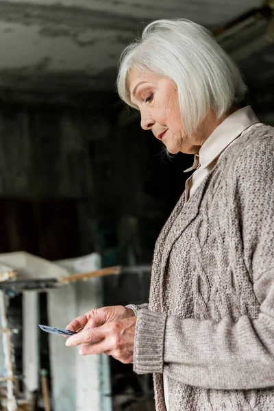 Upset senior woman looking at photo in abandoned school — Stock Photo