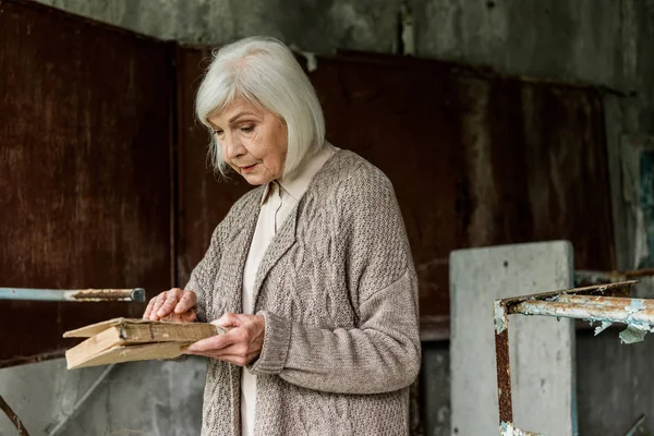 Pripyat, Ukraine - 15. August 2019: Seniorin mit grauen Haaren hält Buch in den Händen — Stockfoto
