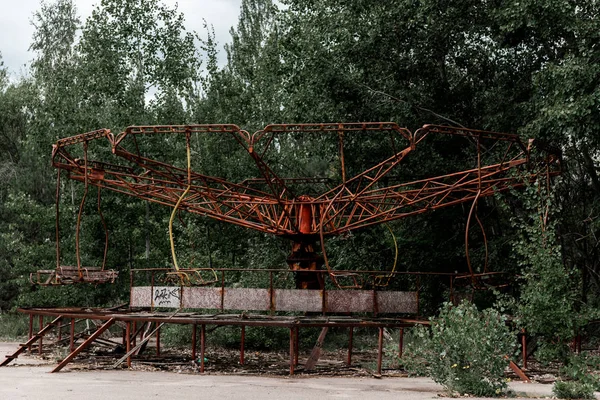 PRIPYAT, UKRAINE - 15 AOÛT 2019 : Carrousel métallique rouge abandonné dans un parc d'attractions vert à Tchernobyl — Photo de stock