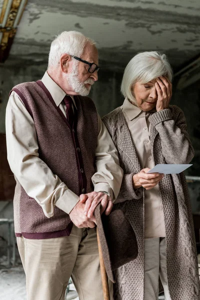 Женщина на пенсии трогает лицо рядом с бородатым мужем, держа фотографию — стоковое фото