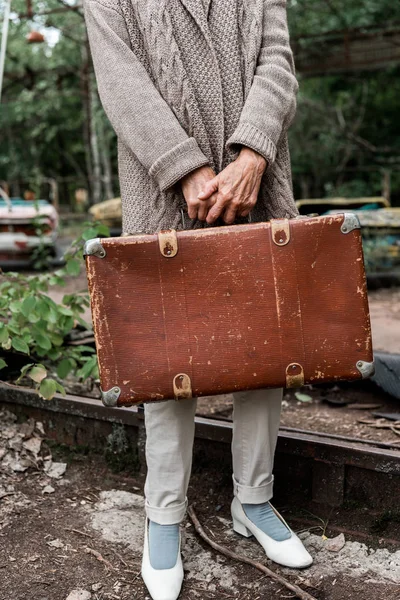 PRIPYAT, UKRAINE - 15 AOÛT 2019 : vue recadrée d'une femme âgée tenant une valise dans un parc d'attractions — Photo de stock