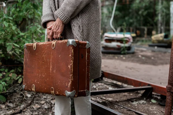 PRIPYAT, UCRANIA - 15 de agosto de 2019: vista recortada de una mujer jubilada sosteniendo una maleta en el parque de atracciones - foto de stock