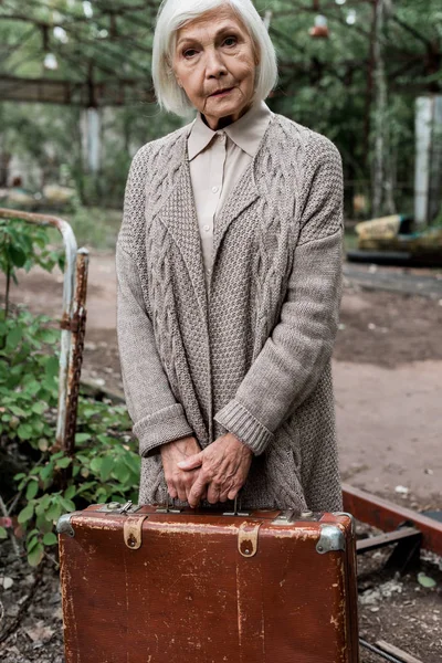 PRIPYAT, UCRANIA - 15 de agosto de 2019: Mujer jubilada con una maleta de pelo gris en el parque de atracciones - foto de stock