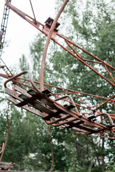 PRIPYAT, UCRANIA - 15 de agosto de 2019: enfoque selectivo del carrusel metálico rojo en el parque de atracciones verde en chernobyl - foto de stock