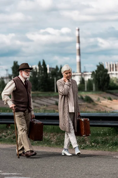PRIPYAT, UKRAINE - AUGUST 15, 2019: senior man and woman walking with luggage near chernobyl nuclear power plant — Stock Photo