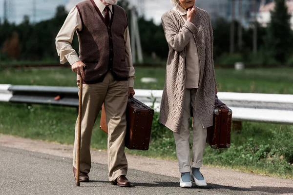 Обрезанный вид на пенсионера и женщину, идущих с дорожными сумками — стоковое фото