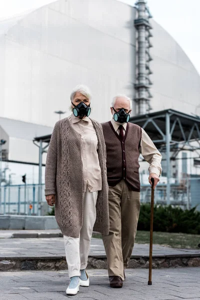 PRIPYAT, UCRANIA - 15 de agosto de 2019: pareja de ancianos con máscaras protectoras de pie cerca del reactor de Chernobyl abandonado - foto de stock