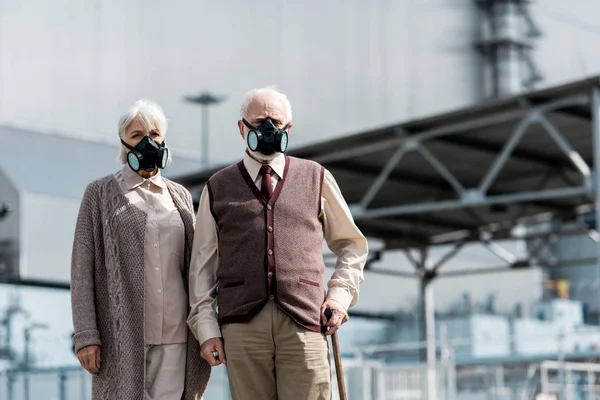 PRIPYAT, UCRAINA - 15 AGOSTO 2019: donna anziana e uomo in maschere protettive in piedi vicino al reattore di Chernobyl abbandonato — Foto stock