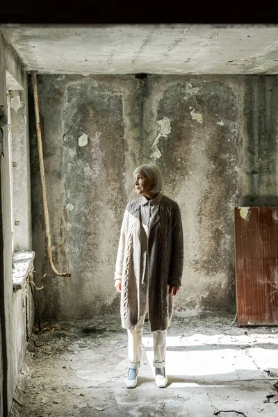 Seniorin mit grauen Haaren steht in leerem und schmutzigem Raum — Stockfoto