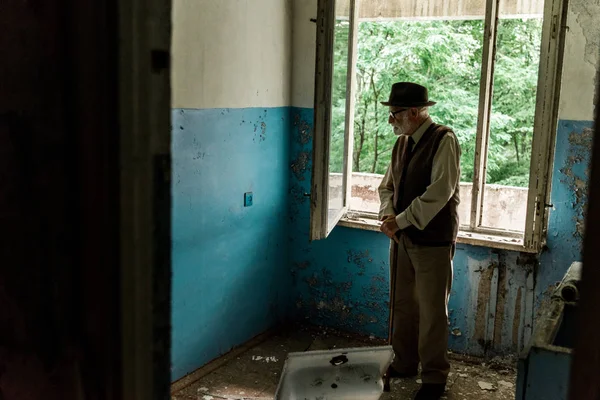 Сумний старший чоловік стоїть у пошкодженій кімнаті — стокове фото