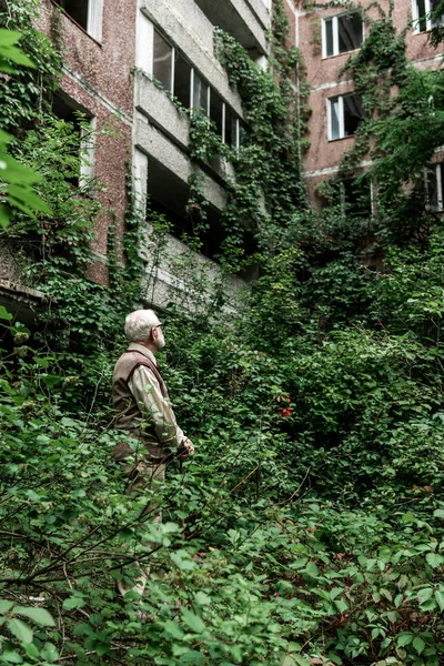 Homme à la retraite dans des lunettes regardant maison envahie de feuilles — Photo de stock