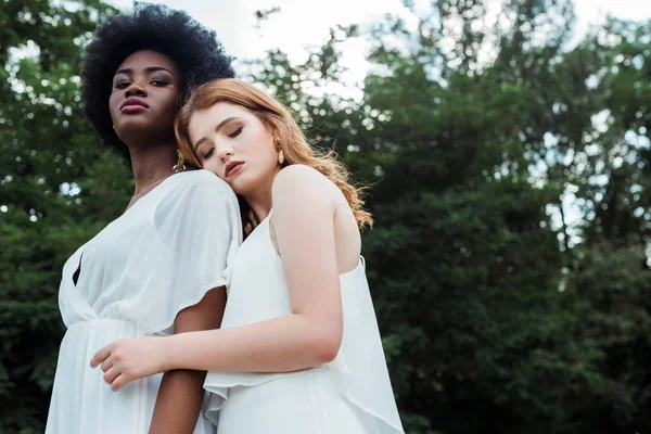 Low angle view of redhead girl hugging african american friend outside — Stock Photo