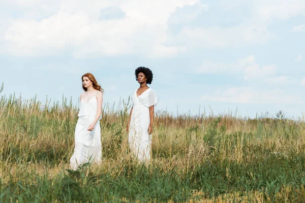 Pretty multicultural girls in dresses walking in field — Stock Photo