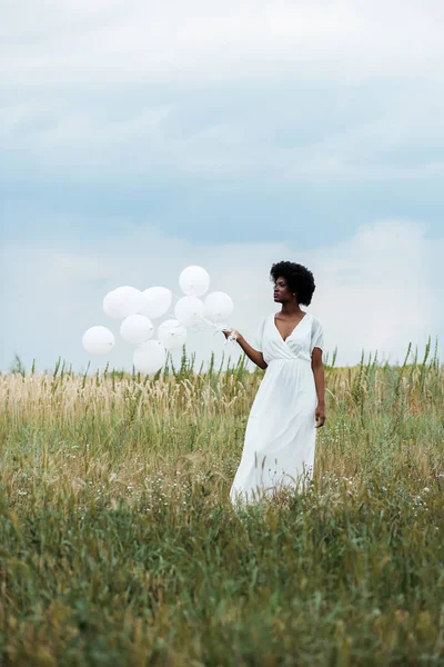 Selektiver Fokus eines afrikanisch-amerikanischen Mädchens im weißen Kleid, das Luftballons im Feld hält — Stockfoto