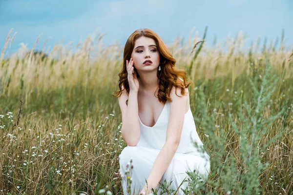 Foyer sélectif de jeune rousse femme en robe blanche assis dans le champ — Photo de stock