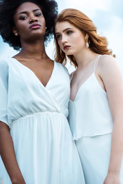 Pretty redhead woman standing with african american girl against sky — Stock Photo